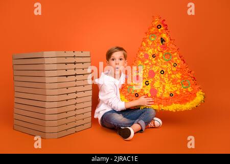 Ganzkörper-Foto von staunenden Jungen sitzen Boden essen riesige Pizza Scheibe isoliert hell lebendige Farbe Hintergrund Stockfoto