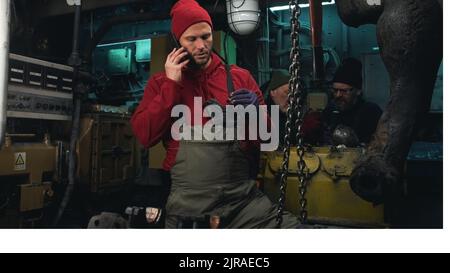 Zoom in der Ansicht eines erwachsenen Mannes, der Metallteile untersucht und sich während der Arbeit im Maschinenraum des Schiffes in der Nähe von Kollegen auf dem Mobiltelefon unterhält Stockfoto