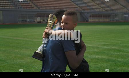 Afroamerikanischer Mann, der nach einem Fußballspiel im Stadion Trophäe übergab und mit einem gemischten Rennjungen sprach Stockfoto