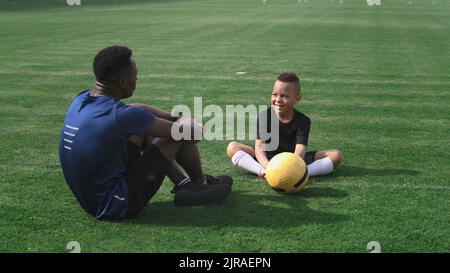 Pan um gemischte Rennen Junge gestikulierend und diskutieren Training mit afroamerikanischen Trainer auf dem Feld Stockfoto