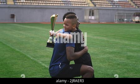 Afroamerikanischer Mann, der nach einem Fußballspiel im Stadion Trophäe übergab und mit einem gemischten Rennjungen sprach Stockfoto