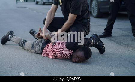 Polizist, der sich dem afroamerikanischen Mann widersetzt, auf den Boden drückt und Handschellen anschnürte Stockfoto