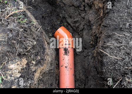 Ein orangefarbenes Kunststoffrohr aus einem Klärbecken mit einem Durchmesser von 160 mm, das in einem Graben liegt. Stockfoto