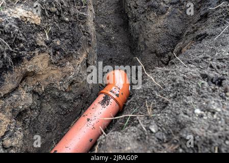 Ein orangefarbenes Kunststoffrohr aus einem Klärbecken mit einem Durchmesser von 160 mm, das in einem Graben liegt. Stockfoto
