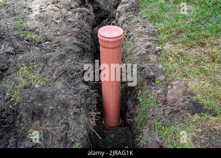 Ein orangefarbenes Kunststoffrohr aus einem Klärbecken mit einem Durchmesser von 160 mm, das in einem Graben liegt, sichtbares Rohr zur Revision. Stockfoto