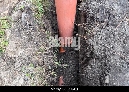 Ein orangefarbenes Kunststoffrohr aus einem Klärbecken mit einem Durchmesser von 160 mm, das in einem Graben liegt, sichtbares Rohr zur Revision. Stockfoto