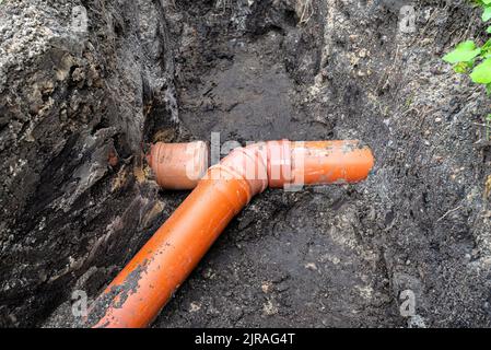 Ein orangefarbenes Kunststoffrohr aus einem Klärbecken mit einem Durchmesser von 160 mm, das in einem Graben liegt, ein blindes Rohr ist sichtbar. Stockfoto