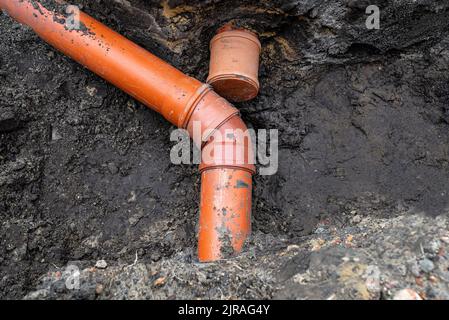 Ein orangefarbenes Kunststoffrohr aus einem Klärbecken mit einem Durchmesser von 160 mm, das in einem Graben liegt, ein blindes Rohr ist sichtbar. Stockfoto