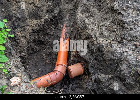 Ein orangefarbenes Kunststoffrohr aus einem Klärbecken mit einem Durchmesser von 160 mm, das in einem Graben liegt, ein blindes Rohr ist sichtbar. Stockfoto