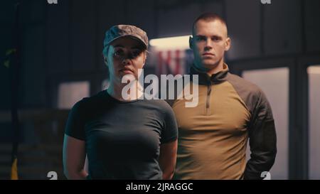 Ansicht einer starken Frau und eines starken Mannes in Sportkleidung, die mit TRX-Seil und US-Flagge im Fitnessstudio auf die Kamera blicken Stockfoto