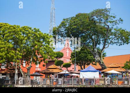 Malacca, Malaysia - 10. August 2022: Blick über den fluss melaka auf den Roten Platz oder den Niederländischen Platz. Die Christuskirche erscheint zwischen den Bäumen. Tou Stockfoto
