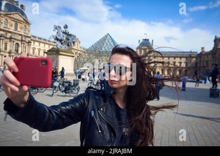 Das Mädchen macht Selfie auf einem Hintergrund eines Louvre in Paris Stockfoto