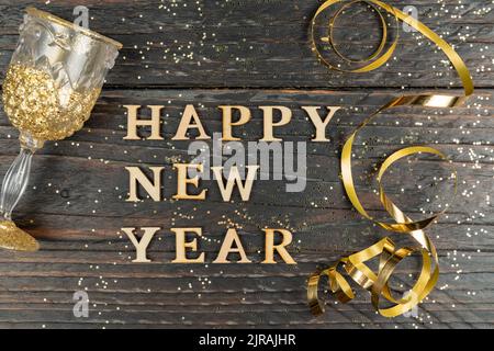 Grußkarte zum neuen Jahr. Ein Glas Champagner und eine goldene Schlange auf einem Holztisch mit verstreuten Konfetti Stockfoto