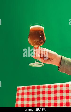 Weibliche Hand hält ein Glas kaltes dunkles Bier auf dunkelgrünem Hintergrund. Oktoberfest, Urlaub, Glück, Festival und Werbekonzept. Stockfoto
