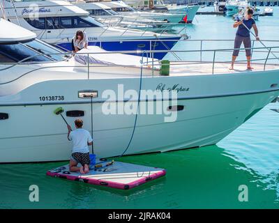 Russland, Sotschi 28.05.2022. Drei Frauen räumen an einem sonnigen Tag eine weiße Yacht auf, die im türkisfarbenen Meer festgemacht ist Stockfoto