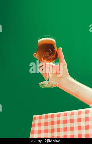 Weibliche Hand hält ein Glas kaltes dunkles Bier auf dunkelgrünem Hintergrund. Oktoberfest, Urlaub, Glück, Festival und Werbekonzept. Stockfoto