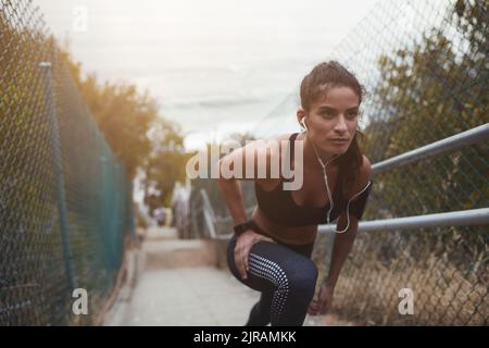 Athletische junge Frau macht Dehnübungen auf einer Treppe im Freien. Sportliche junge Frau, die sich aufwärmt, bevor sie morgens zum Laufen geht. Stockfoto