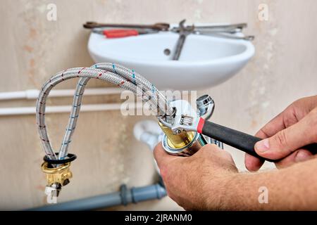 Klempner fixiert geflochtenen Verbindungsschlauch zum Wasserhahn vor der Installation Wasserhahn auf Waschbecken im Badezimmer. Stockfoto