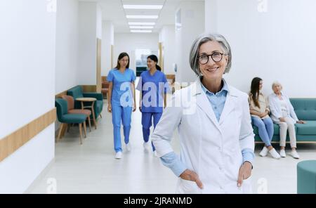 Freundliche Hausärztin in medizinischer Uniform, die während des Arbeitstages in einer modernen medizinischen Klinik steht, Porträt Stockfoto