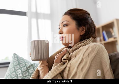 Kranke asiatische Frau trinkt heißen Tee zu Hause Stockfoto