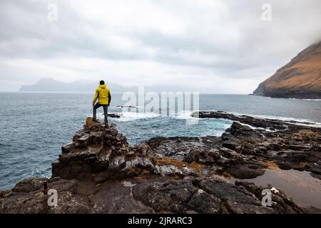 Färöer-Inseln, Eysturoy, Gjogv, männlicher Wanderer, der den Atlantischen Ozean vom Rand der Klippe aus bewundert Stockfoto