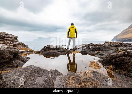 Färöer-Inseln, Eysturoy, Gjogv, männlicher Wanderer, der den Atlantischen Ozean vom Rand der Klippe aus bewundert Stockfoto