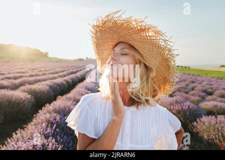 Lächelnde Frau mit geschlossenen Augen, die das Kinn im Lavendelfeld berührt Stockfoto