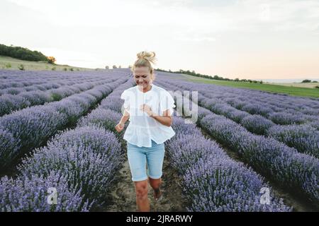 Glückliche Frau, die inmitten von Lavendelpflanzen läuft Stockfoto