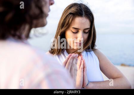Junge Frau meditiert mit Händen umklammert von Freund Stockfoto