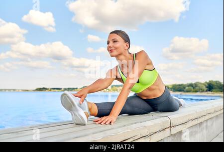 Junge Frau, die sich am Meer komplett aufteilt Stockfoto