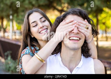 Glückliche junge Frau, die die Augen des Freundes im Park bedeckt Stockfoto