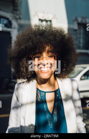 Glückliche Geschäftsfrau mit Afro-Frisur, die an sonnigen Tagen eine Brille trägt Stockfoto