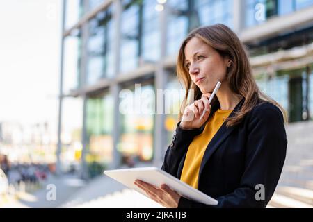 Durchdachte Geschäftsfrau mit der Hand am Kinn, die den Tablet-PC und den digitalisierten Stift hält Stockfoto