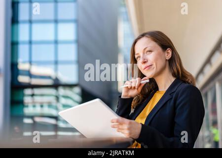 Lächelnde Geschäftsfrau mit der Hand auf dem Kinn, die den Tablet-PC hält Stockfoto