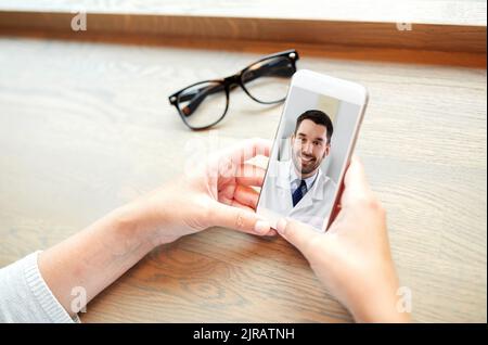 Hände einer Frau, die das Telefon hält, mit dem Arzt auf dem Bildschirm Stockfoto