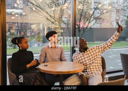 Glücklicher junger Mann, der Selfie mit Freunden über das Smartphone macht Stockfoto