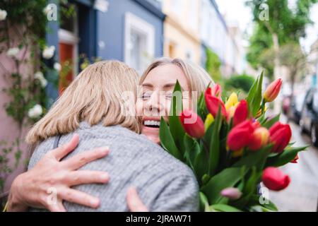 Glückliche ältere Frau mit Blumen umarmen Tochter Stockfoto