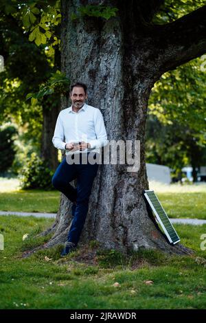 Lächelnder Geschäftsmann, der das Smartphone vor dem Solarpanel im Park hält Stockfoto