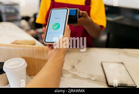 Hand des Kunden, der kontaktlos über das Smartphone im Café bezahlt Stockfoto