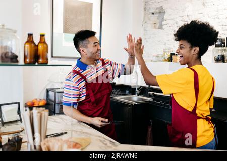 Glücklicher Mann und Frau, die sich im Coffee Shop hoch-fünf geben Stockfoto