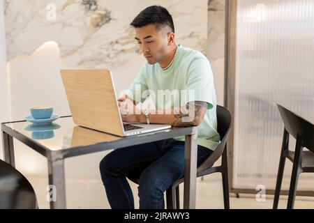 Junger Mann, der mit einem Laptop am Tisch im Café sitzt Stockfoto