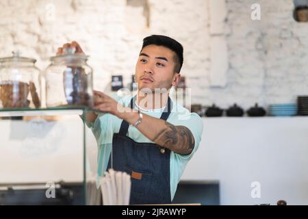 Junger Mann mit Schürze, der im Café arbeitet Stockfoto