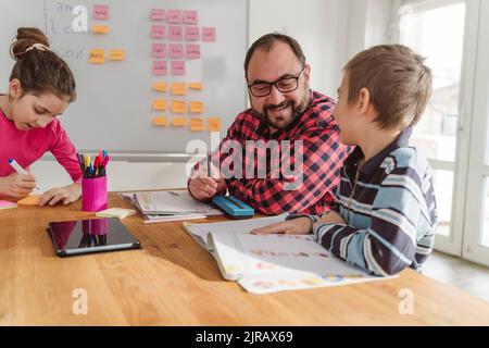 Lächelnder Lehrer Unterricht Junge mit Buch am Tisch Stockfoto