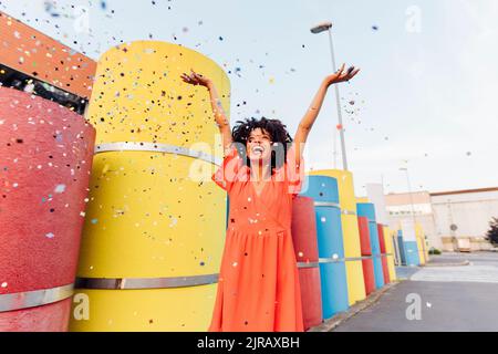 Verspielte Frau, die Konfetti durch mehrfarbige Pfeifen wirft Stockfoto