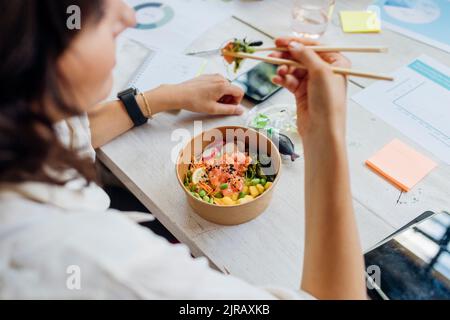 Geschäftsfrau, die in der Mittagspause im Büro einen gesunden Sack mit Essstäbchen isst Stockfoto