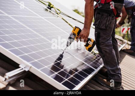 Elektriker mit Elektrowerkzeug für die Installation von Solarpanel auf dem Dach Stockfoto
