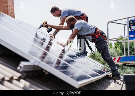 Handwerker installieren Sonnenkollektoren auf dem Dach des Hauses Stockfoto