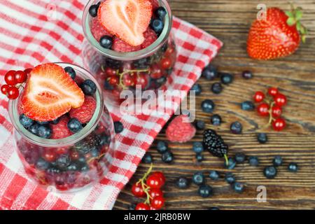 Gemischte Beeren in einem Glas auf braunem Holzgrund Stockfoto