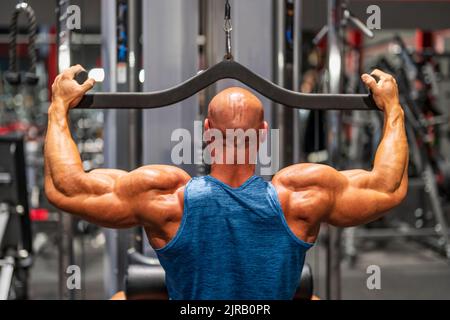 Muskulöser Bodybuilder mit lat Pulldown-Maschine im Fitnessstudio Stockfoto