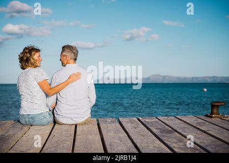 Glückliches Paar, das Zeit miteinander verbringt, auf dem Steg zu sitzen Stockfoto